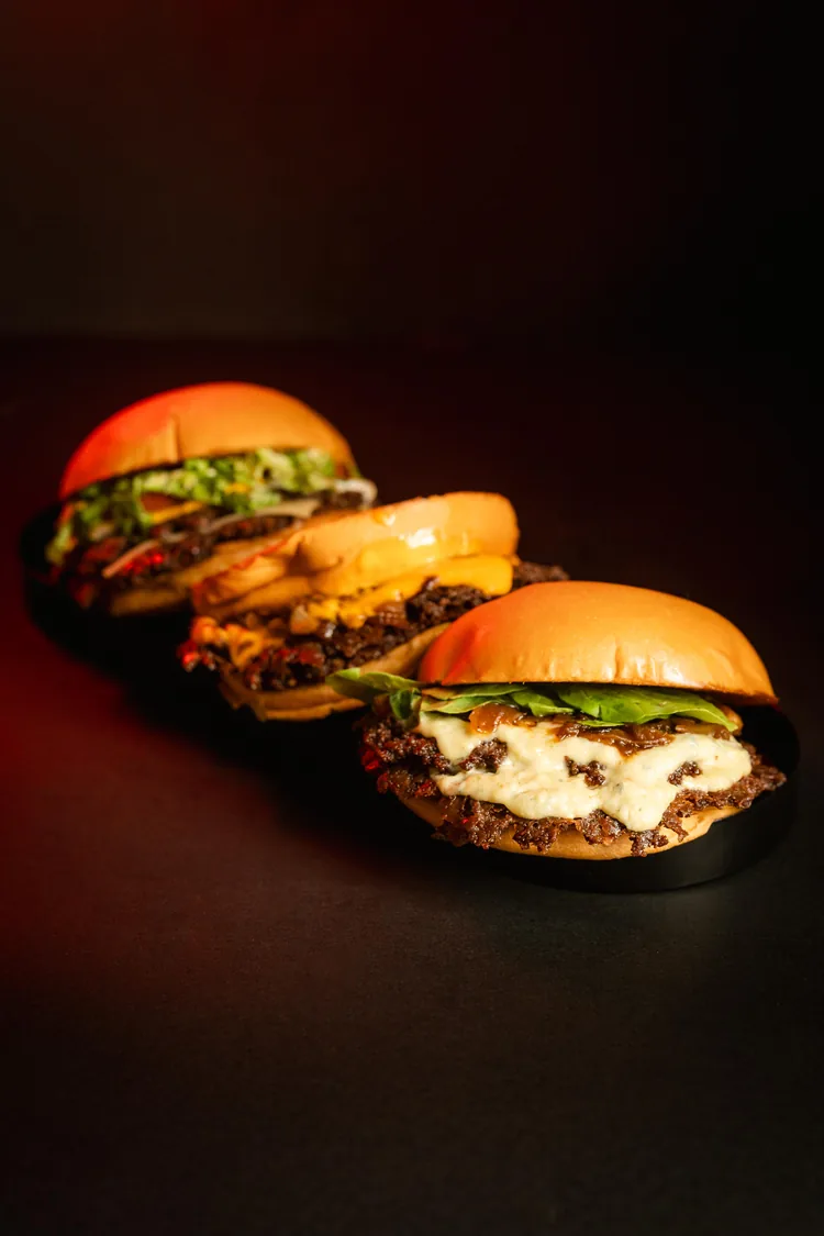 Tres hamburguesas alineadas en fila sobre una bandeja oscura