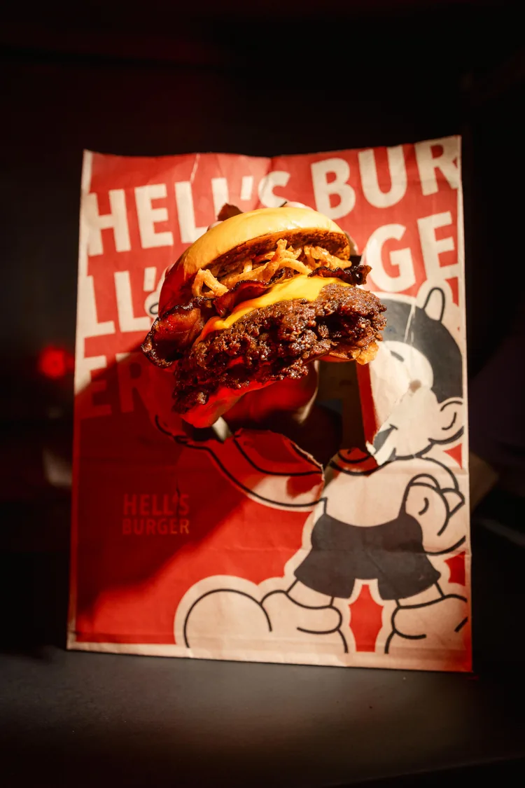 Una hamburguesa doble con cheddar apoyada sobre una bolsa roja de Hell’s Burger